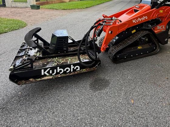 Kubota brush cutter attachment mounted on the track loader, with cut leaves on the deck.